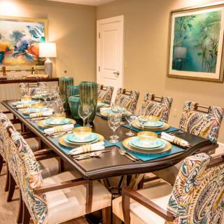 A well-decorated dining room featuring a large table set for a meal, with vibrant artwork on the walls and elegant glassware.