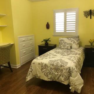A cozy bedroom with yellow walls featuring a single bed and floral bedding, complemented by a wooden floor and functional furniture.