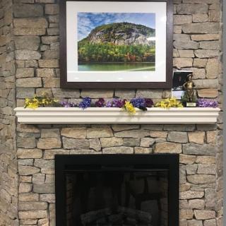 A stone fireplace with a decorated mantel and a framed landscape photo.