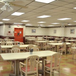 An empty cafeteria with rows of tables and chairs under a tiled ceiling.