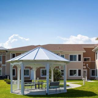 A scenic view of a white gazebo in a garden setting with a modern building in the background on a sunny day.