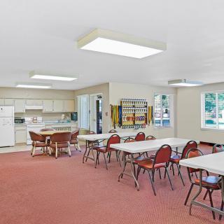 A spacious community center meeting room with a kitchen area, set up with tables and chairs.
