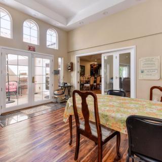 A spacious dining room with wooden floors, featuring a table and chairs, illuminated by natural light through large French doors.