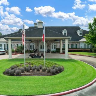 A well-maintained building with flags in front and a circular driveway surrounded by lush grass under a partly cloudy sky.