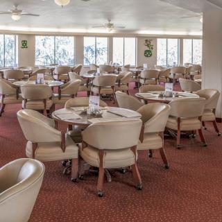An empty dining area with round tables and cushioned chairs on a carpeted floor.