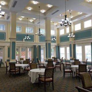 A spacious and elegant dining room with beautifully arranged tables, chairs, chandeliers, and large windows.