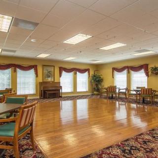 A spacious room with hardwood flooring, featuring tables and chairs, a piano, and large windows with curtains.