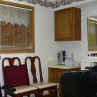 A small room with wooden chairs, a mirror, and a window with blinds.