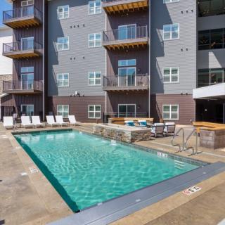 An outdoor swimming pool area with adjacent sun loungers and a modern apartment building in the background.