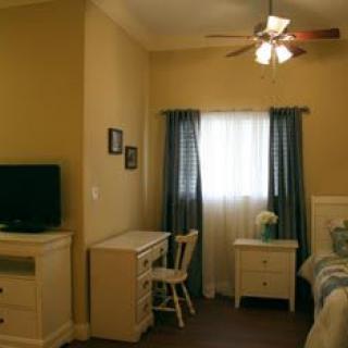 A cozy bedroom featuring a desk, TV, bed, and window with curtains.