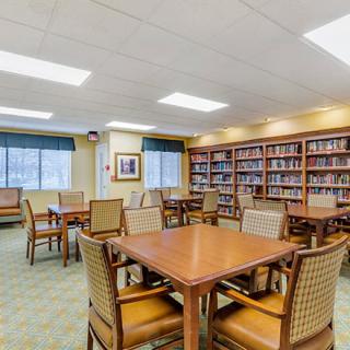 A library interior with tables and chairs, surrounded by bookshelves.