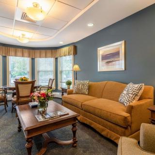 A cozy living room with a brown sofa, wooden coffee table, and large windows adorned with drapes.