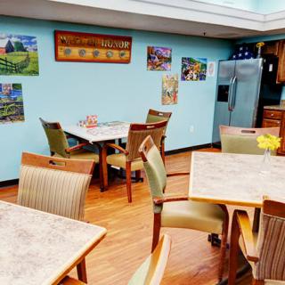 A cozy dining area featuring tables and chairs, decorated with paintings on the walls and a refrigerator in the corner.