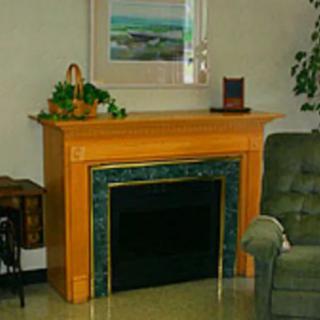 A cozy living room features a wooden fireplace mantel with decorative items and a framed painting above.