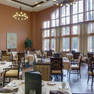 A spacious restaurant dining area with elegant tables and chairs, large windows, and a chandelier.