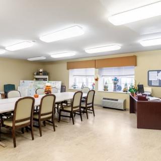 A spacious meeting room with a large conference table surrounded by chairs and lit by fluorescent lights.