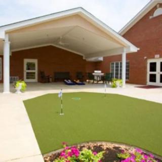 A cozy outdoor patio featuring a putting green, surrounded by flowers and sheltered by a large awning.