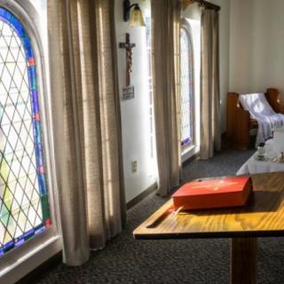 A serene church interior featuring stained glass windows, an altar with a red book, and wooden pews.