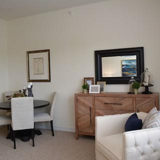A modern living room with a dining area, featuring a wooden sideboard with a mirror above it and elegant decor elements.