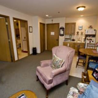 A cozy apartment living room with a pink armchair and a kitchenette.
