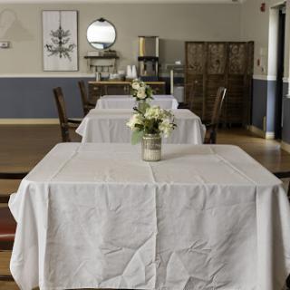 An elegantly set dining area featuring tables with white tablecloths and a floral centerpiece, creating a serene atmosphere.