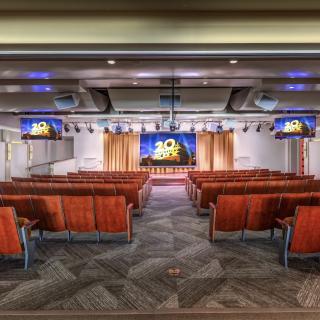 A spacious auditorium with red seating and a stage, equipped with television screens for presentations.