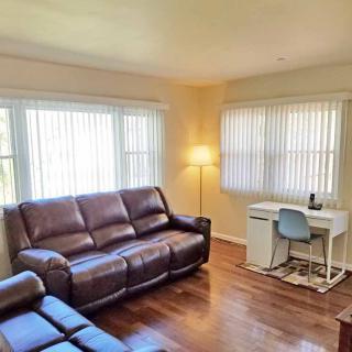A cozy living room with a leather sofa, a desk, and ample natural light from multiple windows.