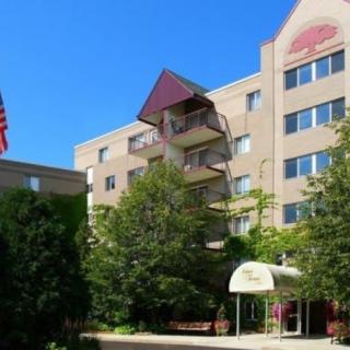 A multistory residential apartment building with balconies and surrounding trees, featuring an American flag at the entrance.