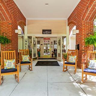 A welcoming entrance to a building with brick walls, featuring several rocking chairs and decorative plants.