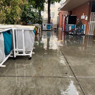 A rain-soaked pathway with storage bins and a bicycle near a building.