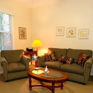A cozy living room with a sofa, armchair, and a coffee table, softly lit by a lamp in the corner.