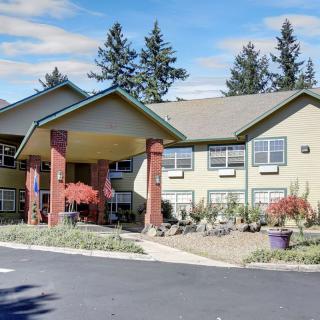 A two-story residential building with a landscaped entrance and trees in the background.