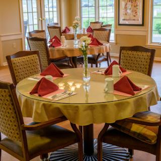 A beautifully arranged dining area ready for guests, featuring elegant table settings with red napkins and a floral centerpiece.