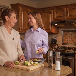 Two women happily preparing food together in a kitchen.