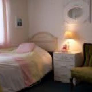 A cozy bedroom with a bed, nightstand, lamp, and chair.