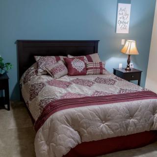 A cozy bedroom with neatly made bed and decorative pillows, flanked by nightstands and a lamp.