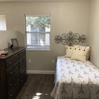 A cozy, minimalistic bedroom with a single bed and dresser, bathed in natural light from the window.