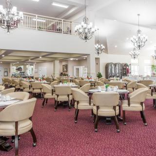A spacious dining area with elegant chandeliers, carpeted floors, and neatly arranged tables and chairs.