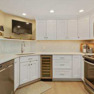 A modern kitchen with white cabinets and stainless steel appliances, featuring a wine cooler integrated into the cabinetry.