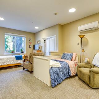 A cozy and well-furnished bedroom interior with two beds, chairs, a window, and a lamp.