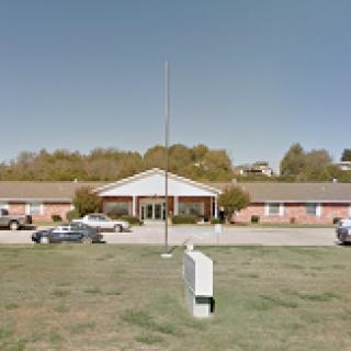 A view of a single-story residential facility with a parking lot and a flagpole out front.