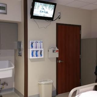 A view of a hospital patient room featuring a television, a door, and medical equipment.