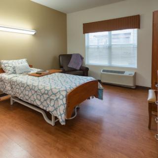 A well-lit hospital room featuring a single bed, comfortable chair, and window.
