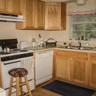 A cozy kitchen with wooden cabinets, featuring an oven, dishwasher, and a window overlooking the outside.