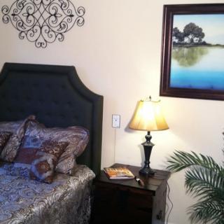 A cozy bedroom corner featuring a bed with patterned pillows, a nightstand with a lamp, and wall art.