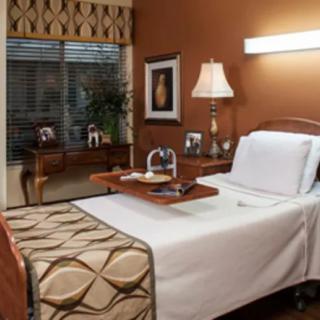 A clean and well-organized hospital room with a bed, bedside table, lamp, and window.