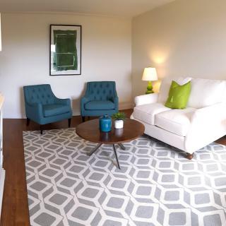 A modern living room with teal armchairs, a white sofa, and geometric patterned rug.