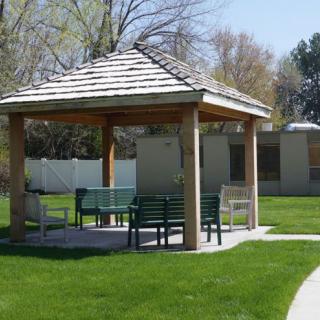 A peaceful park setting with a gazebo and benches surrounded by grass and trees.