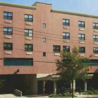 A multi-story brick building with numerous windows, surrounded by trees in an urban setting.