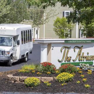 A shuttle bus parked near a landscaped sign for 'The Atrium'.